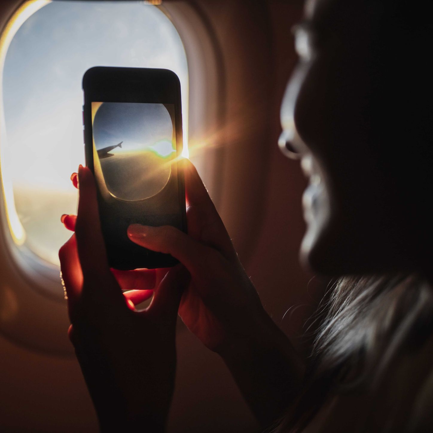 Person photographing a sunrise through an airplane window with a smartphone during a flight.