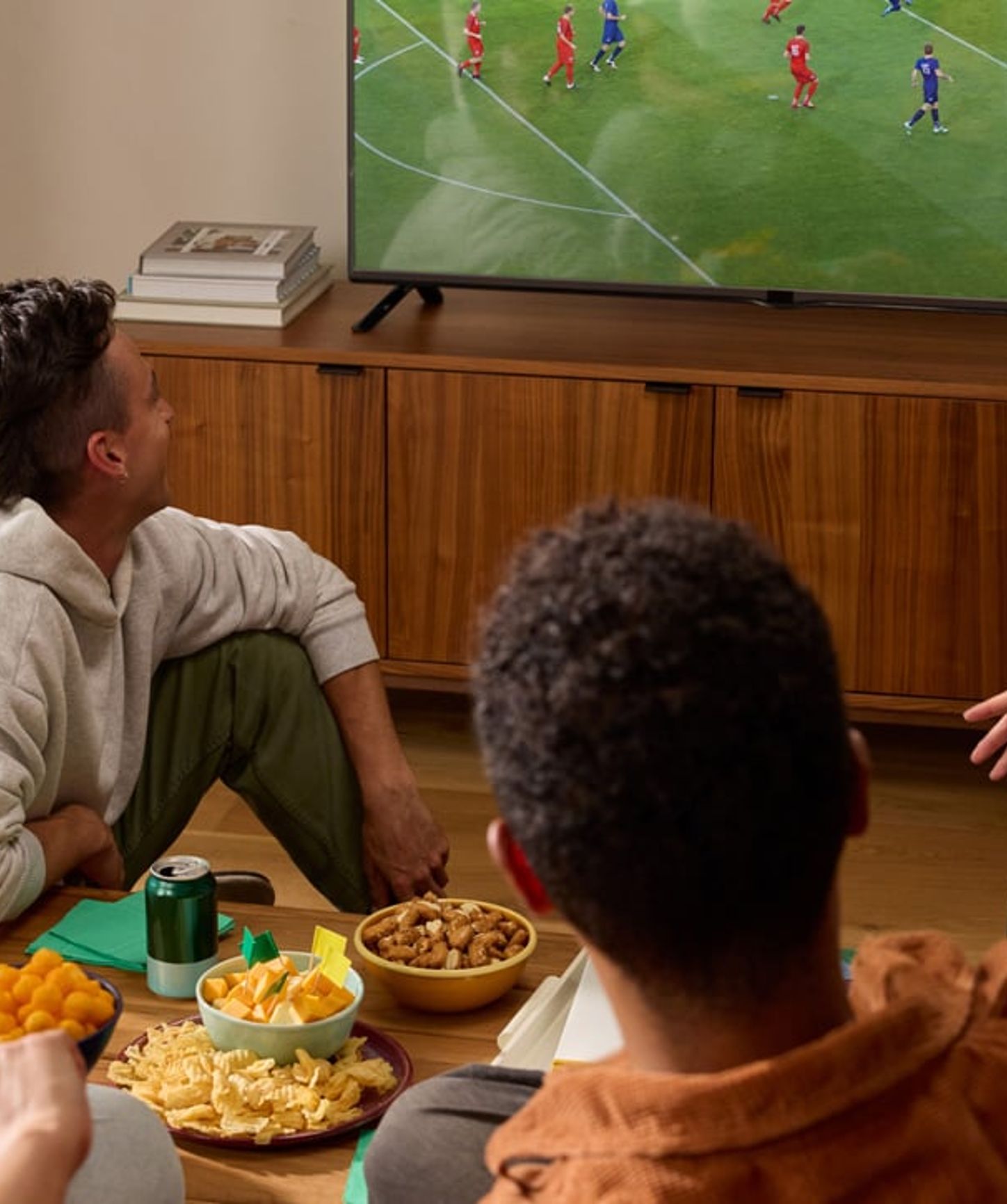 Groupe d'amis regardant un match de football à la télévision tout en dégustant des encas et des boissons dans un salon confortable.