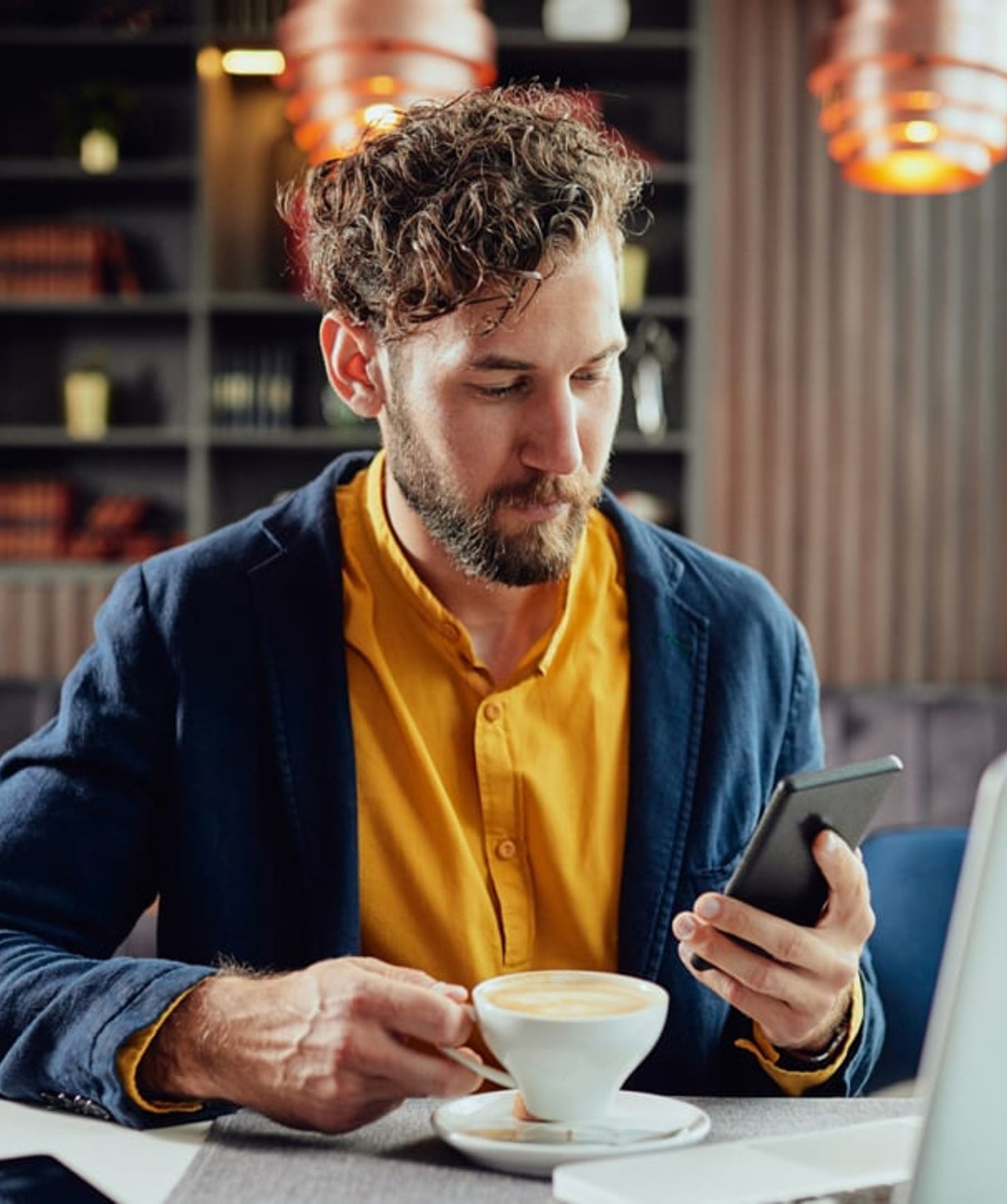 Homme assis dans un café élégant, sirotant un café tout en consultant son smartphone dans un cadre décontracté