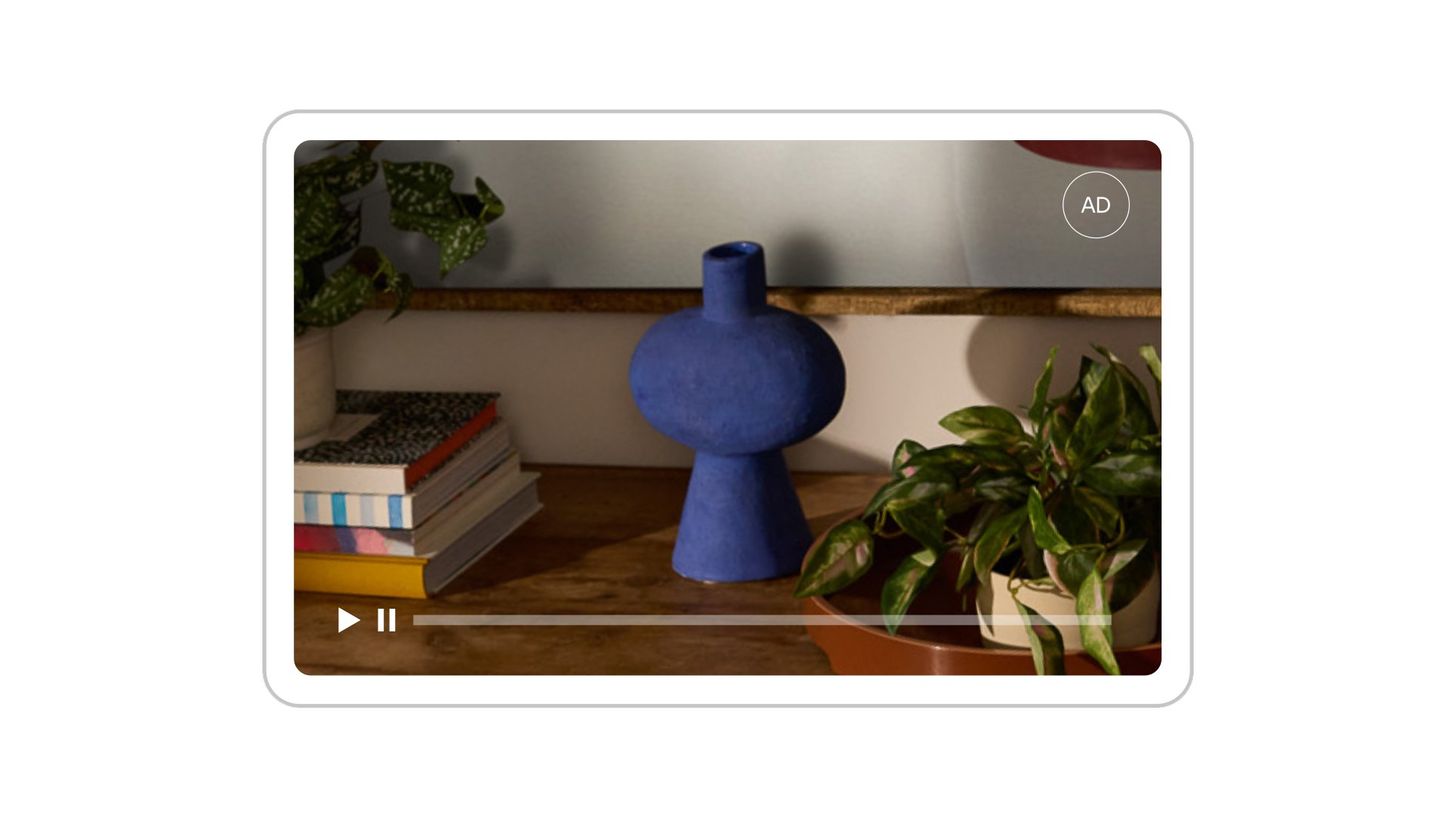 Un anuncio de vídeo en pausa en la pantalla de una tablet muestra un jarrón azul sobre una superficie de madera rodeado de libros y plantas en macetas.
