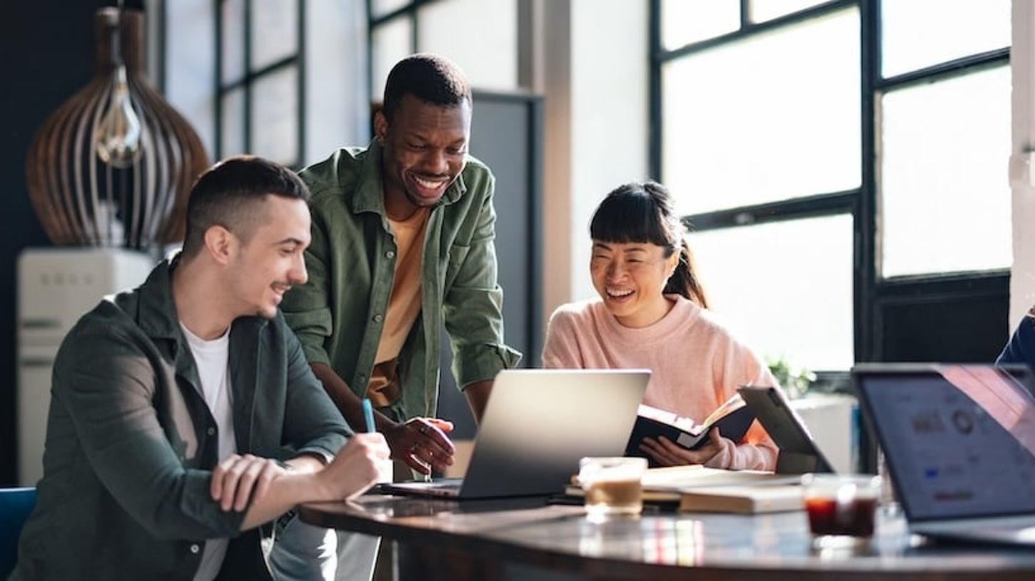 Collaborative team working together in a modern office, gathered around laptops and books in a bright, open workspace