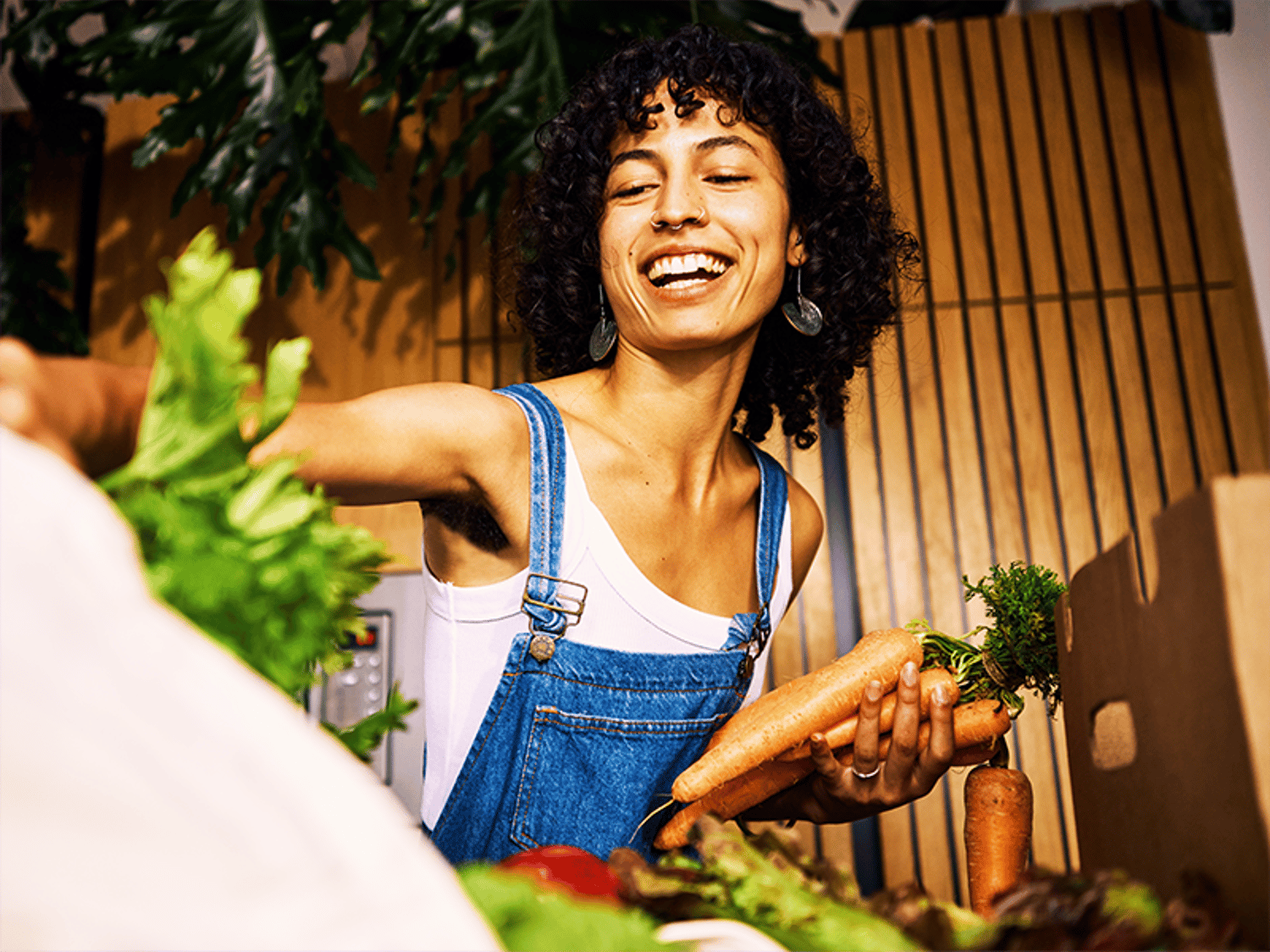 A woman wearing overalls, smiling and shopping for produce