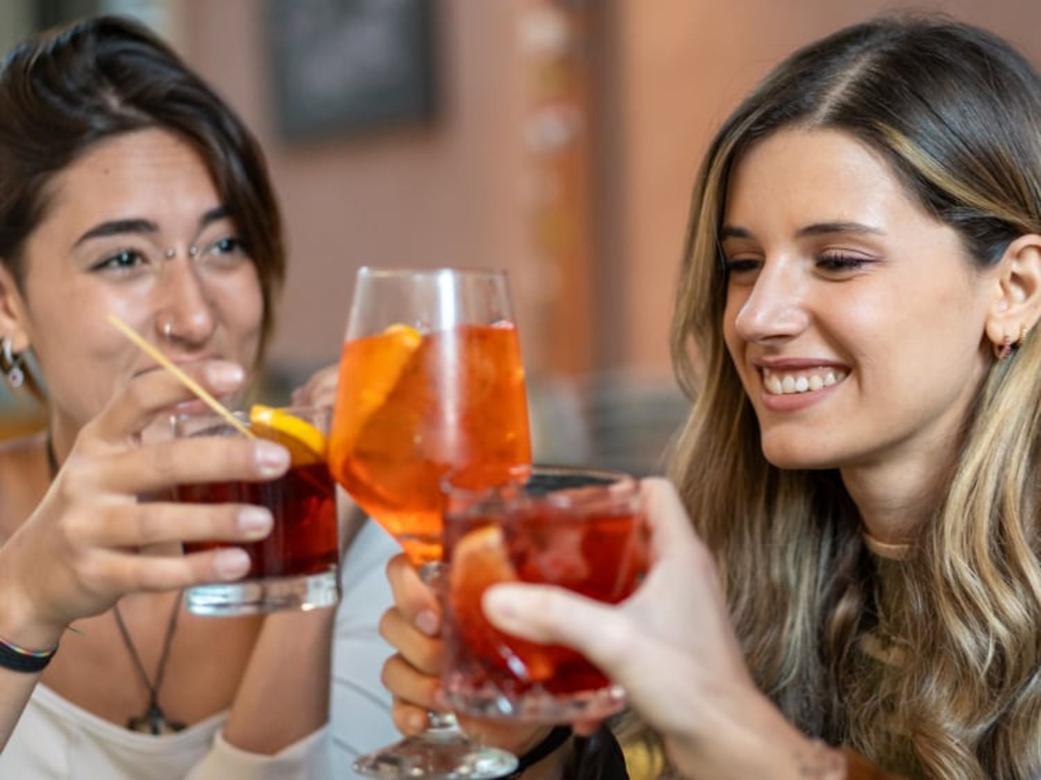Two people smiling and clinking glasses filled with colorful cocktails in a relaxed social setting.