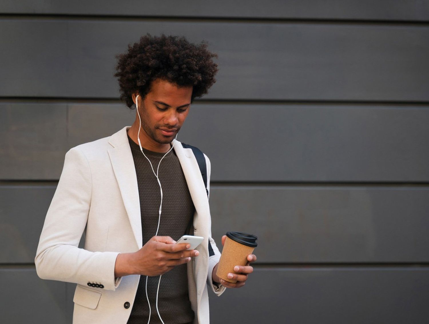 Man looking down at his phone and holding a coffee