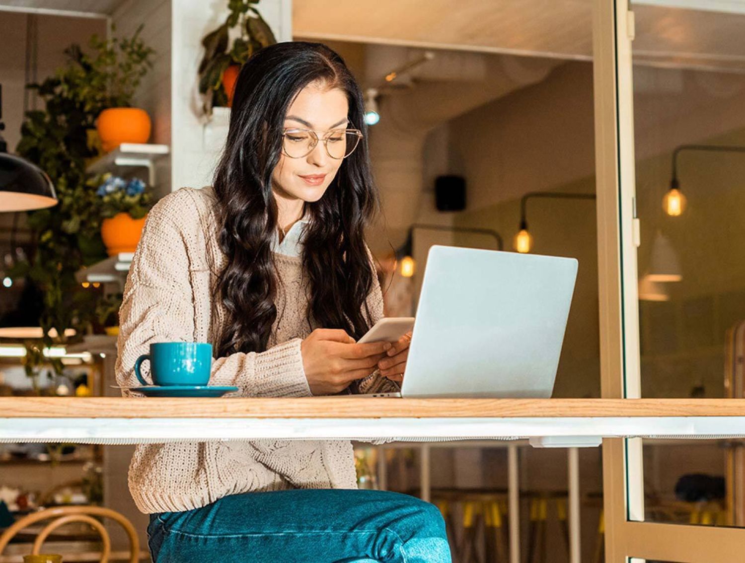 Woman sitting at a table with her laptop, looking at her phone