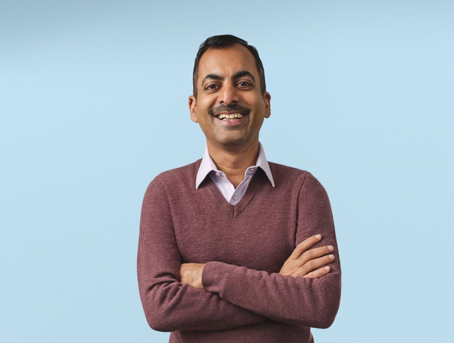 Man in front of a blue background with his arms crossed and smiling