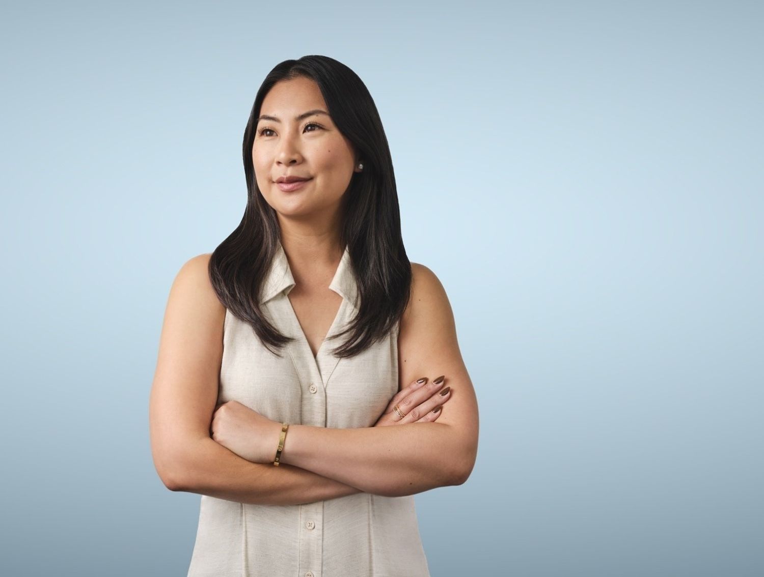 Woman in front of a blue background looking off into the distance with her arms crossed