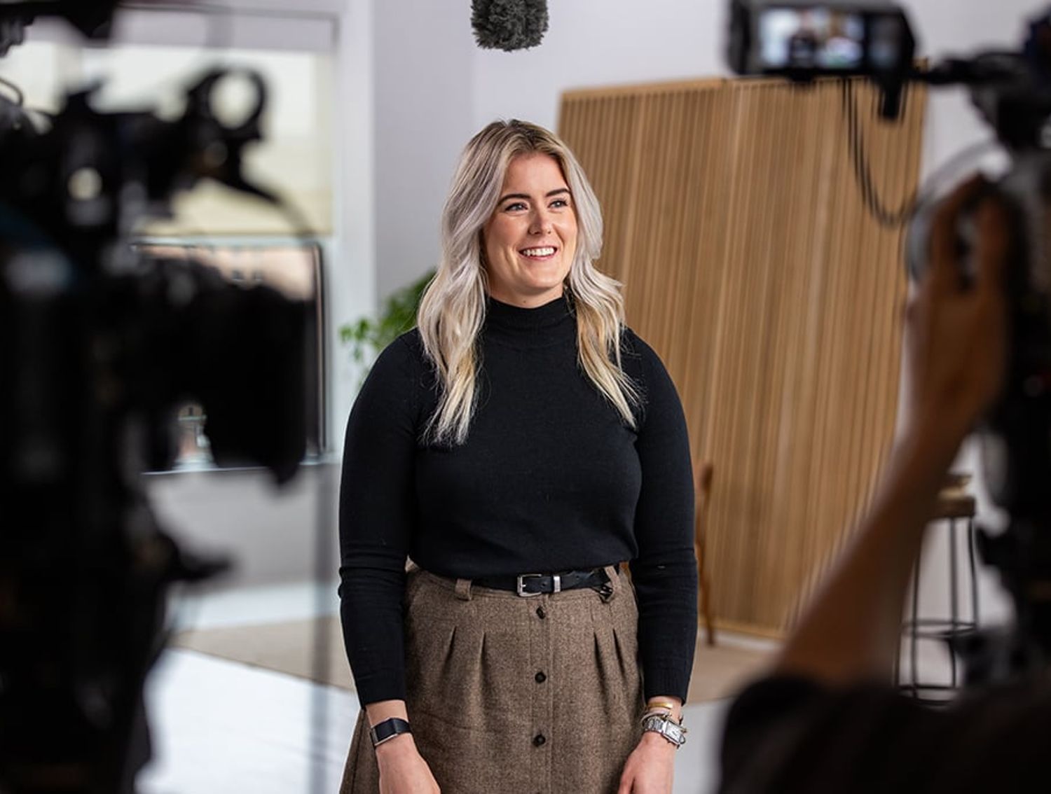 Person standing between cameras during filmed interview setup in modern indoor studio.