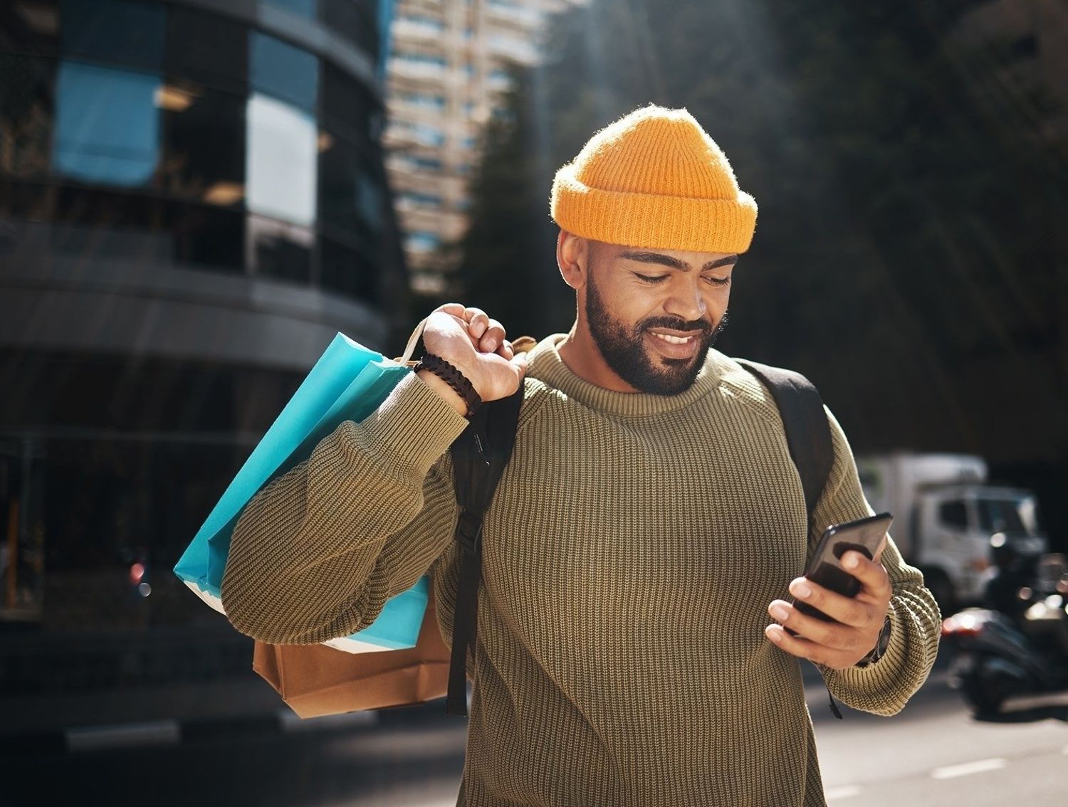 Man in a yellow beanie with shopping bags, looking at his phone