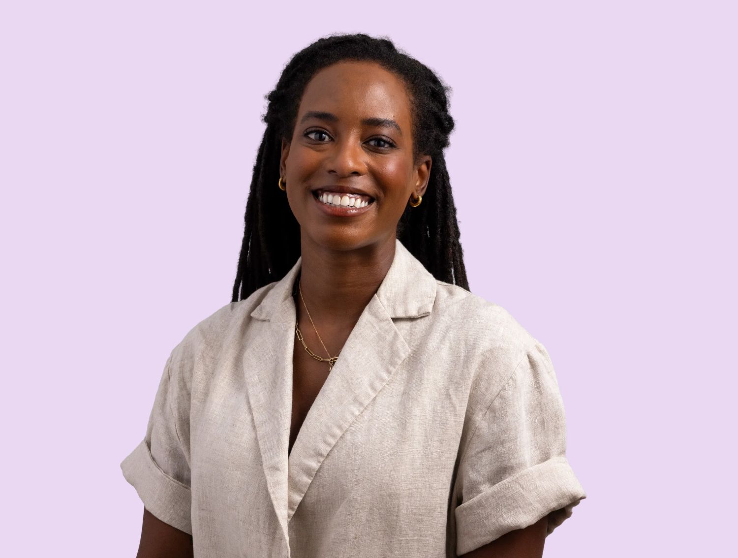 A woman smiling at the camera in front of a lavender backdrop.