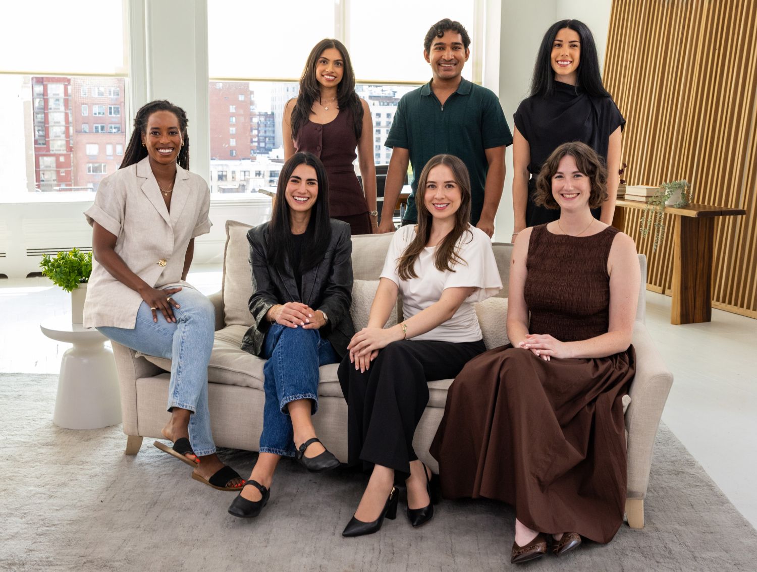 A group of people sitting on or standing behind a couch, and smiling at the camera.
