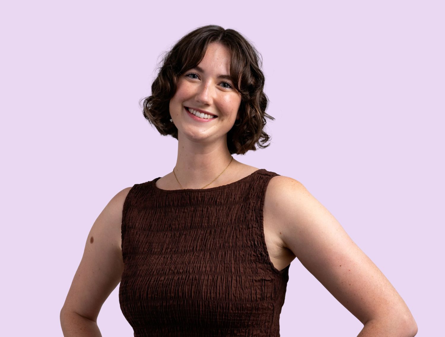 A woman smiling at the camera in front of a lavender backdrop.