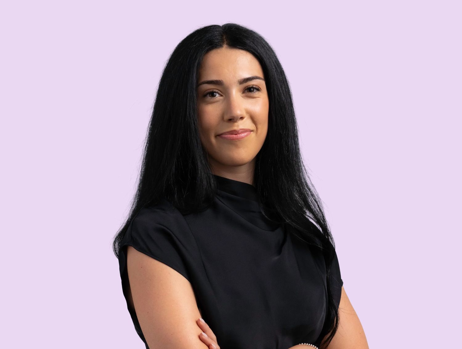A woman smiling at the camera in front of a lavender backdrop.