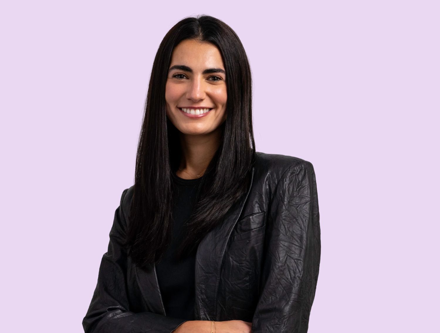 A woman smiling at the camera in front of a lavender backdrop.