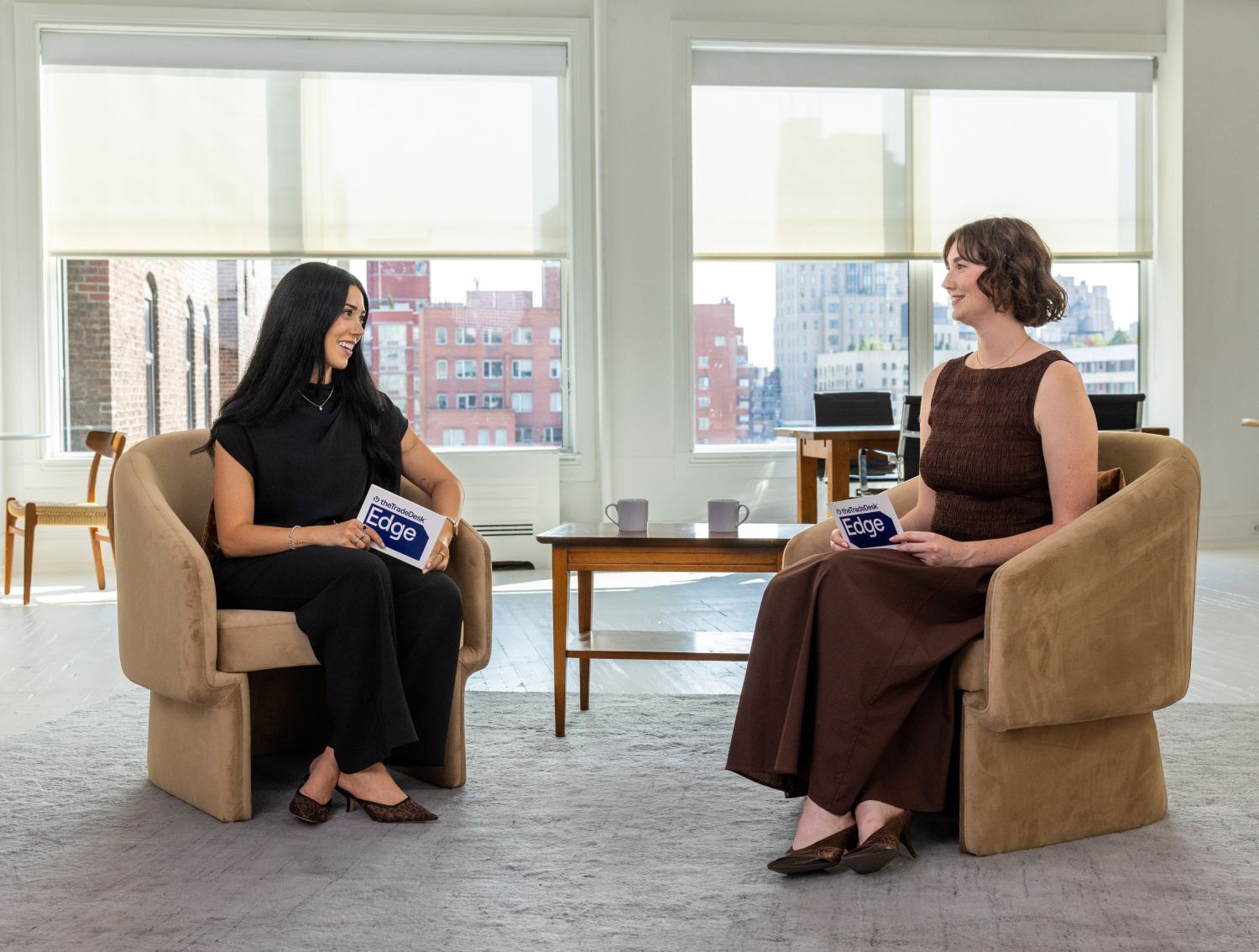 Two women in separate brown upholstered chairs having a discussion and reading queue cards.