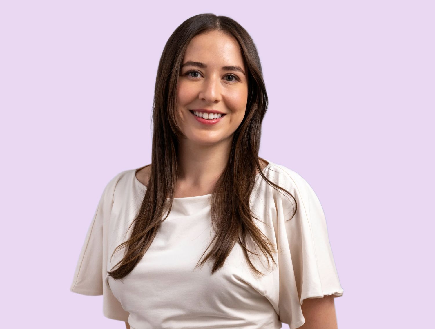 A woman smiling at the camera in front of a lavender backdrop.