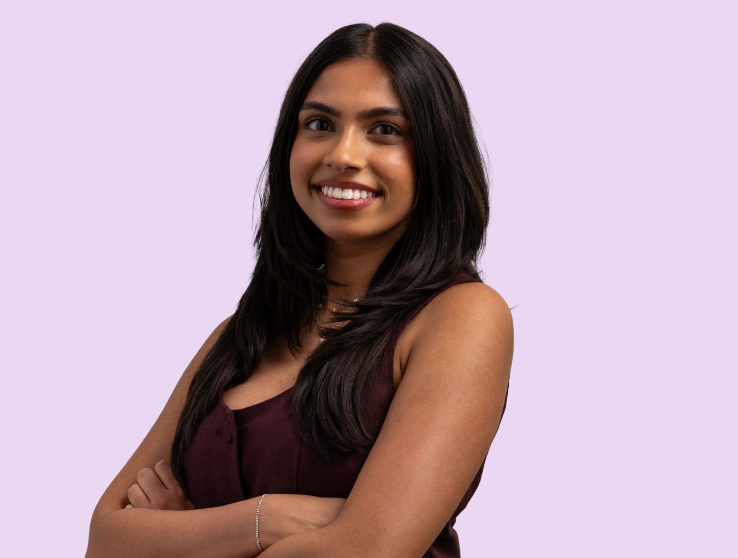 A woman smiling at the camera in front of a lavender backdrop.