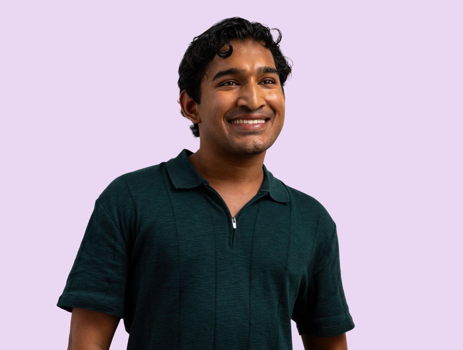 A man smiling at the camera in front of a lavender backdrop.