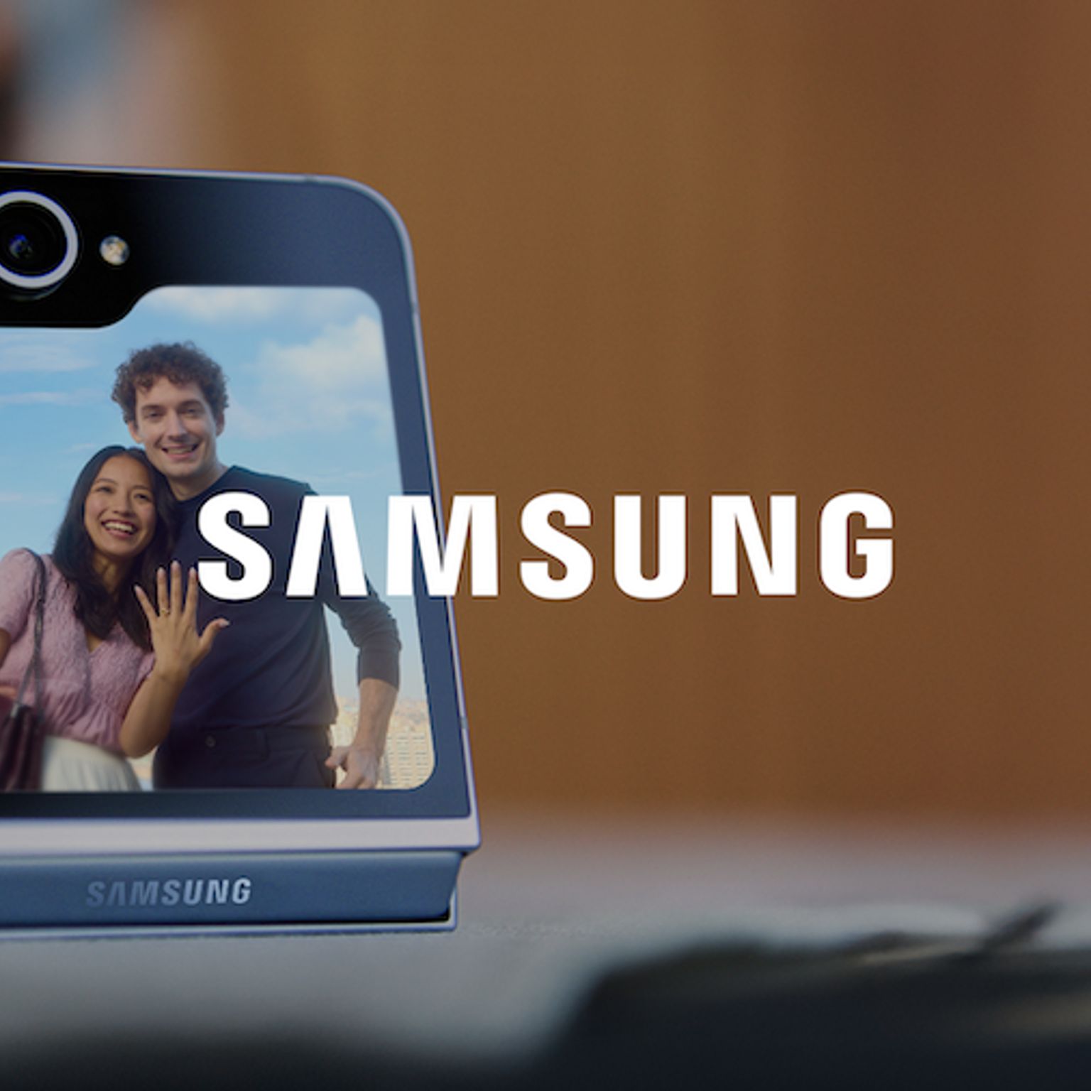 Logo von Samsung vor dem Hintergrundbild eines faltbaren Samsung-Telefons, das ein frisch verlobtes Paar zeigt