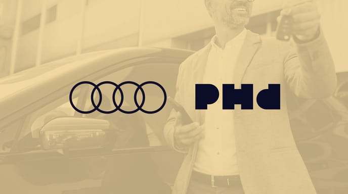 Smiling man in a beige blazer holding car keys and a smartphone while standing next to a black car outside a modern building.