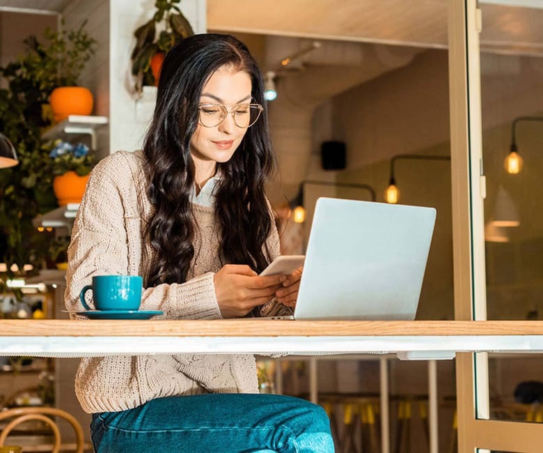Woman sitting at a table with her laptop, looking at her phone