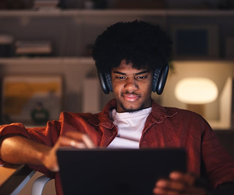 Person wearing headphones using tablet in dimly lit room, representing digital media consumption.