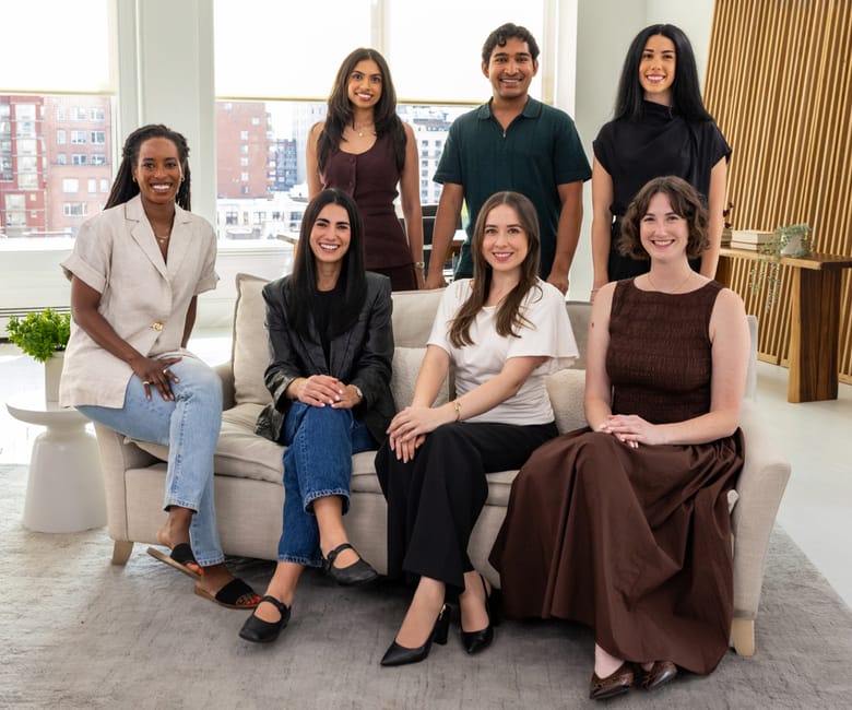 A group of people sitting on or standing behind a couch, and smiling at the camera.