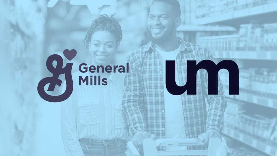 Smiling adult couple shopping together in a grocery store aisle, pushing a cart filled with items.