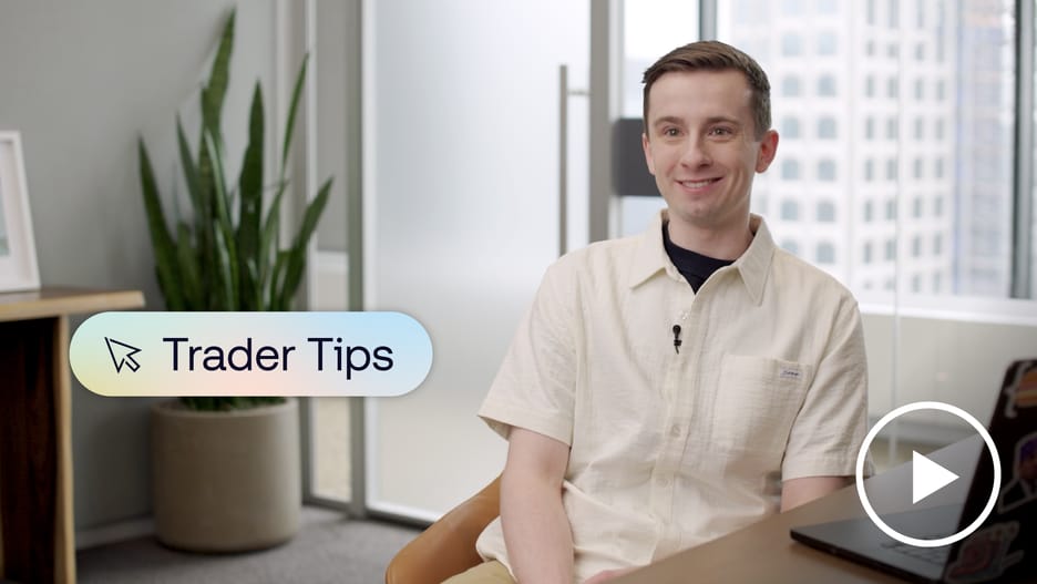 Candid image of a trader smiling at the camera while sitting at his desk with his laptop open. A banner on screen reads “Trader Tips."