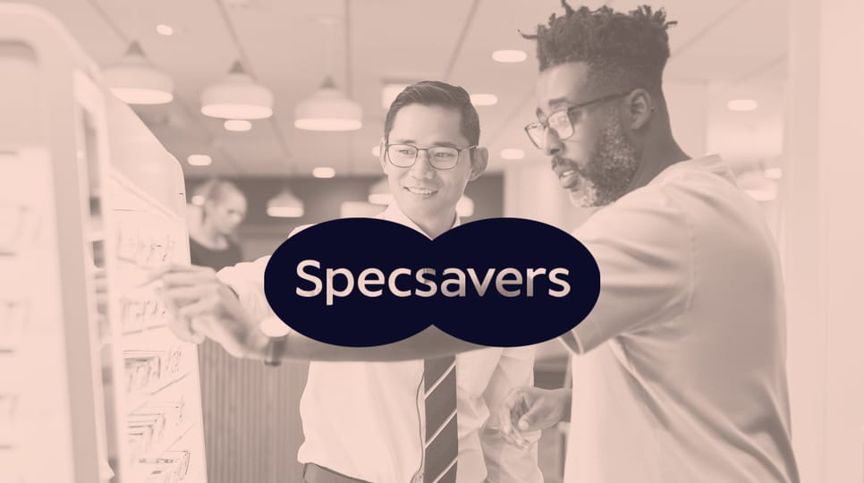 Two people wearing glasses at eyeglass store picking out lenses with the Specsavers logo in the middle of the image