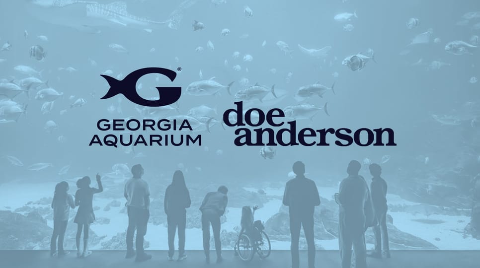 People looking into an aquarium tank filled with fish and Georgia Aquarium and Doe Anderson logos in the center