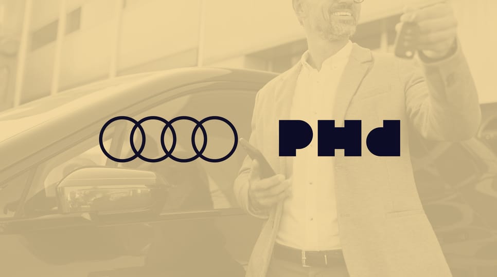 Smiling man in a beige blazer holding car keys and a smartphone while standing next to a black car outside a modern building.