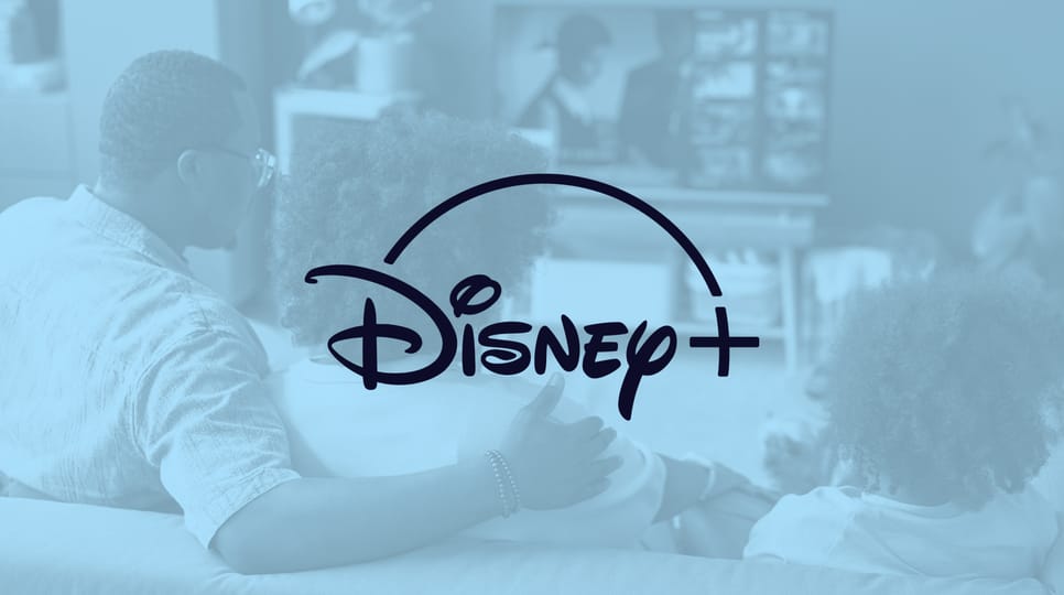 A family sits on a couch watching TV with a light blue overlay and the Disney+ logo displayed over top.