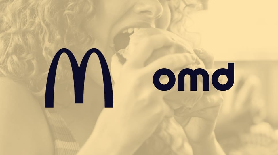Close-up of a person with curly red hair taking a bite of a sandwich, smiling in a bright, casual setting.