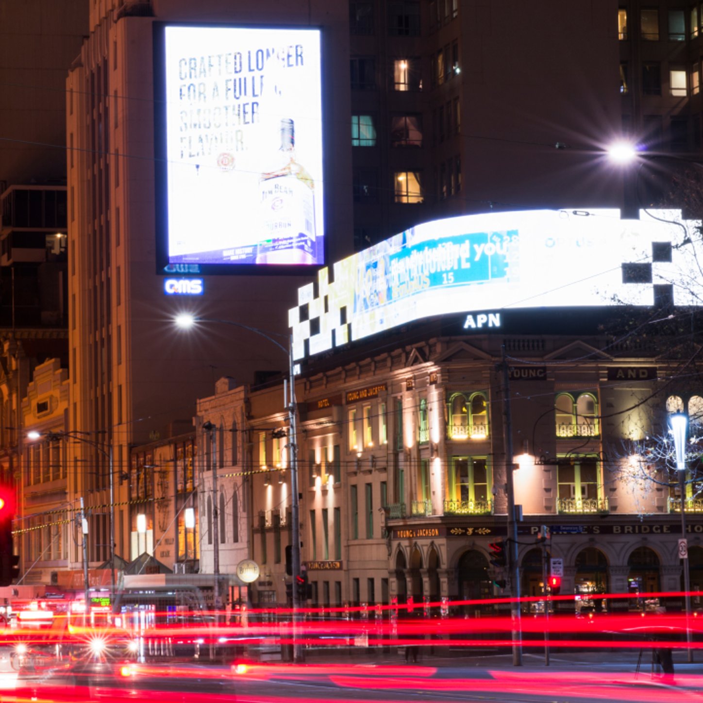 A nighttime cityscape features large digital billboards illuminating a busy street, capturing the dynamic energy of out-of-home advertising in an urban environment.