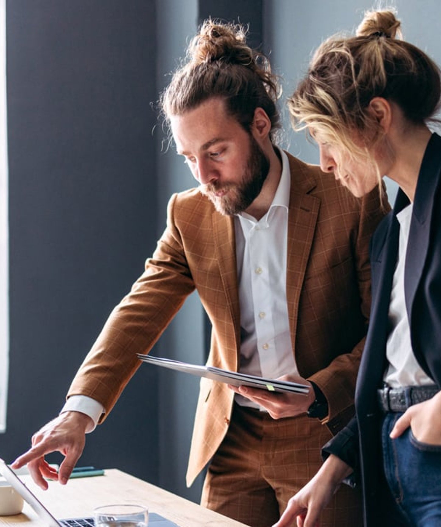 Two professionals collaborating in a modern office, reviewing information on a laptop and discussing strategy