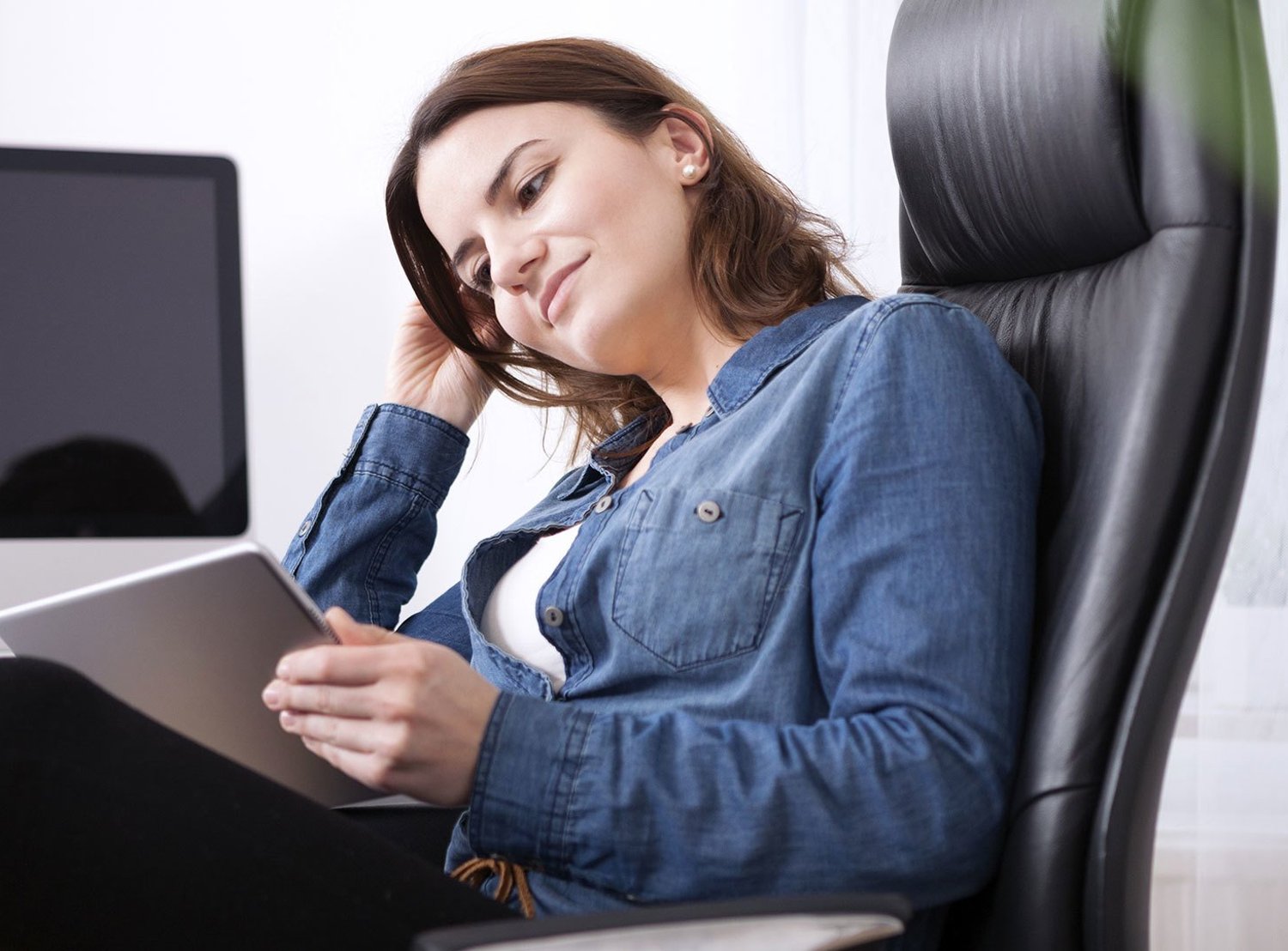 Woman sitting in a black office chair looking at her tablet