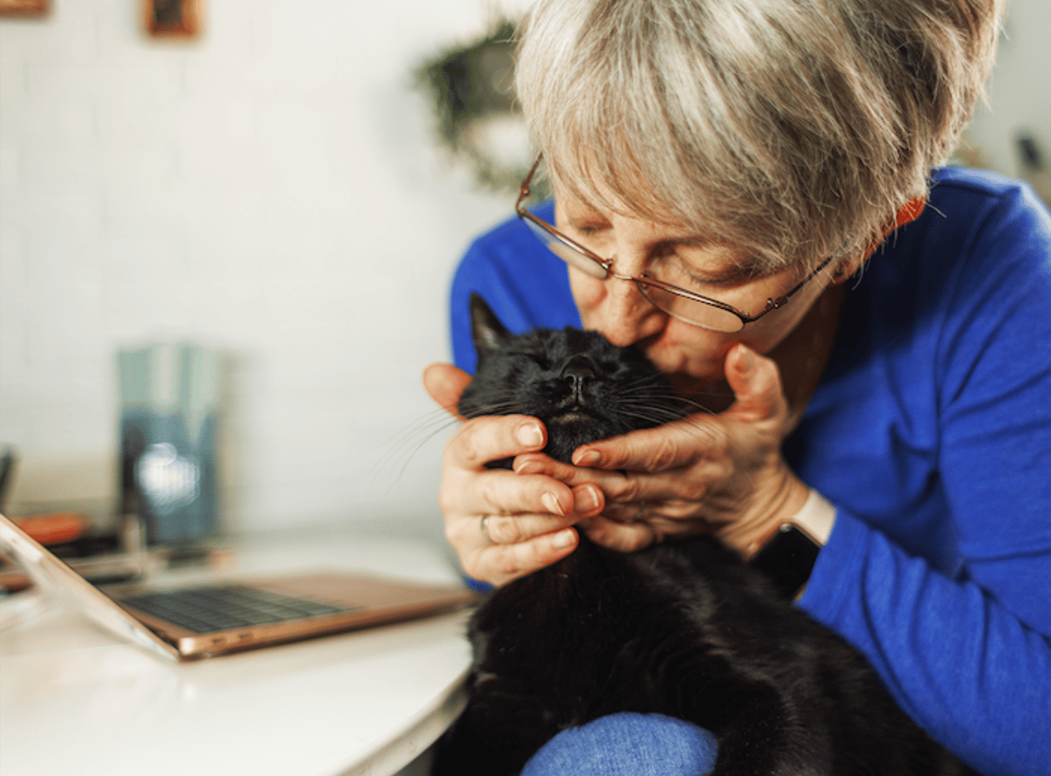 Image shows a woman kissing her black cat