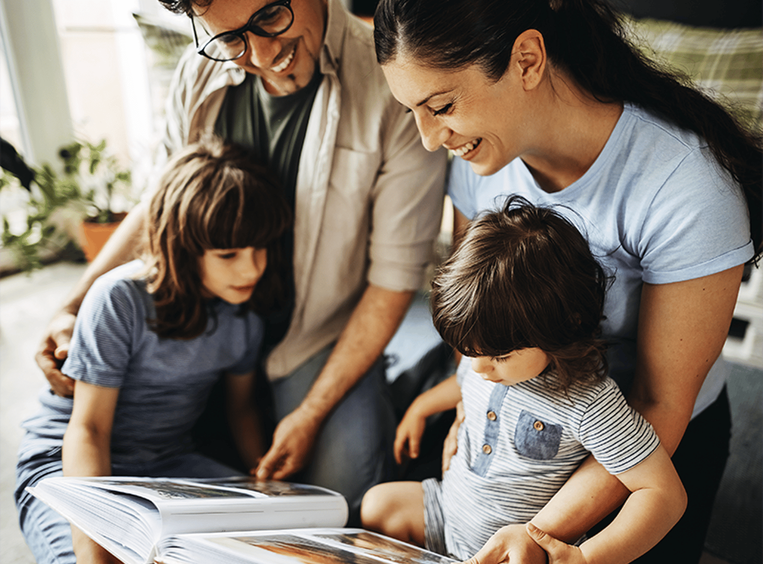 A happy family of four sitting together, smiling and looking at a book.