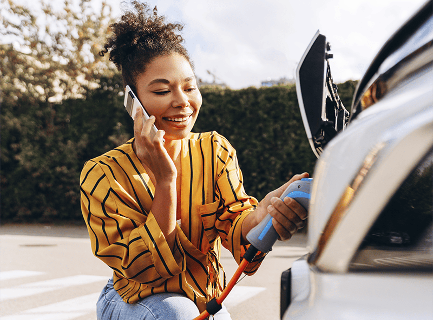 A smiling woman on the phone while charging an electric vehicle.