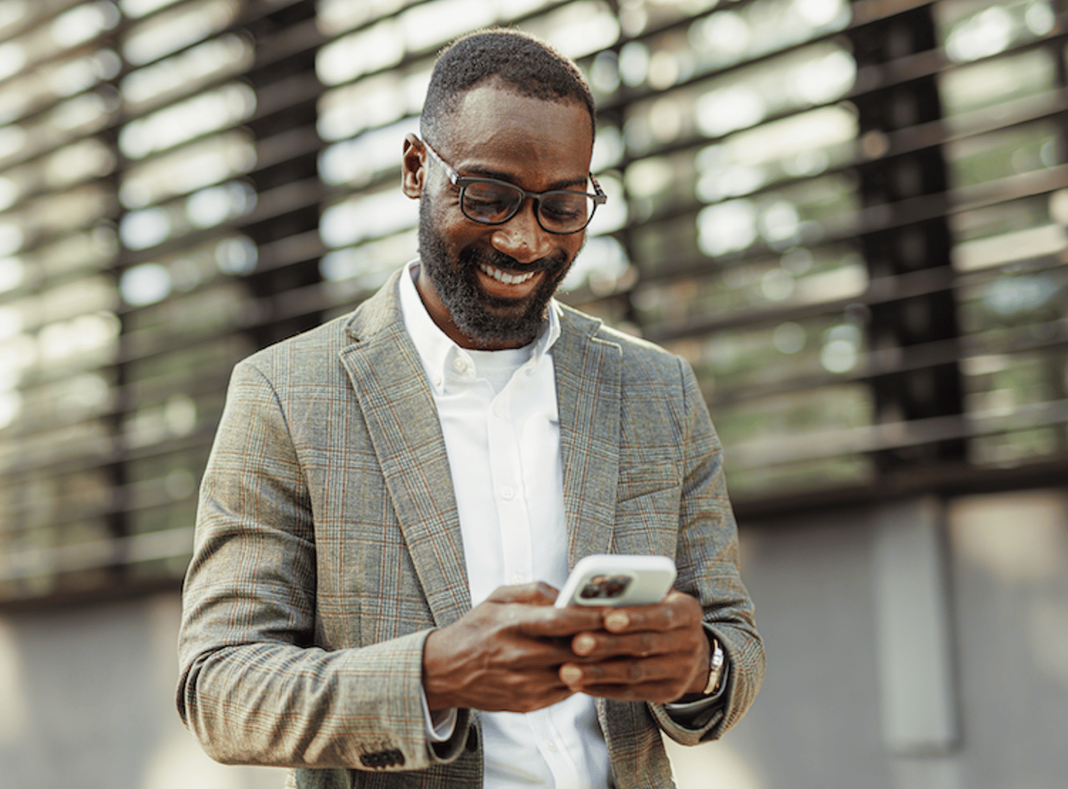 Image shows a man smiling and texting on his phone