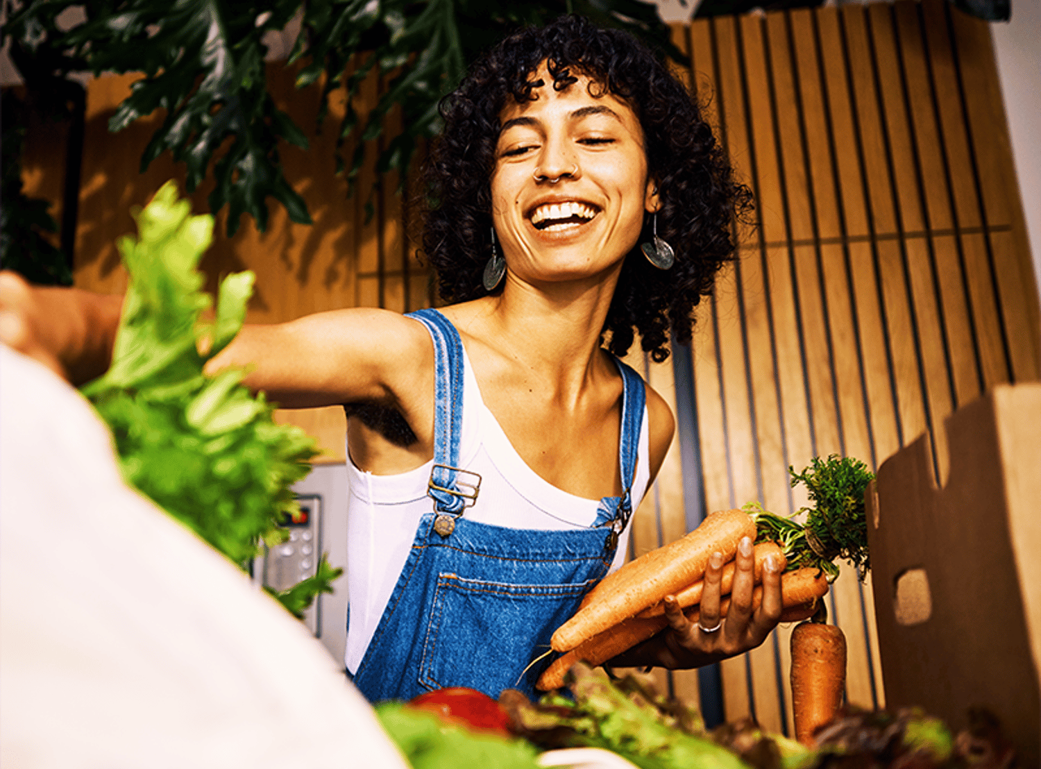 A woman wearing overalls, smiling and shopping for produce