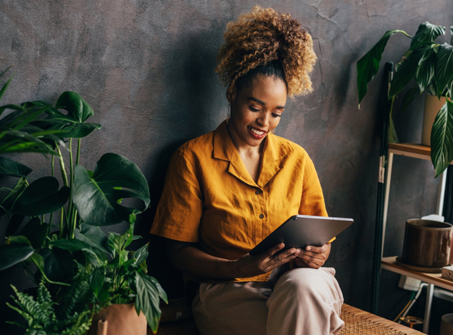 Woman in a yellow shirt sitting and looking at her tablet