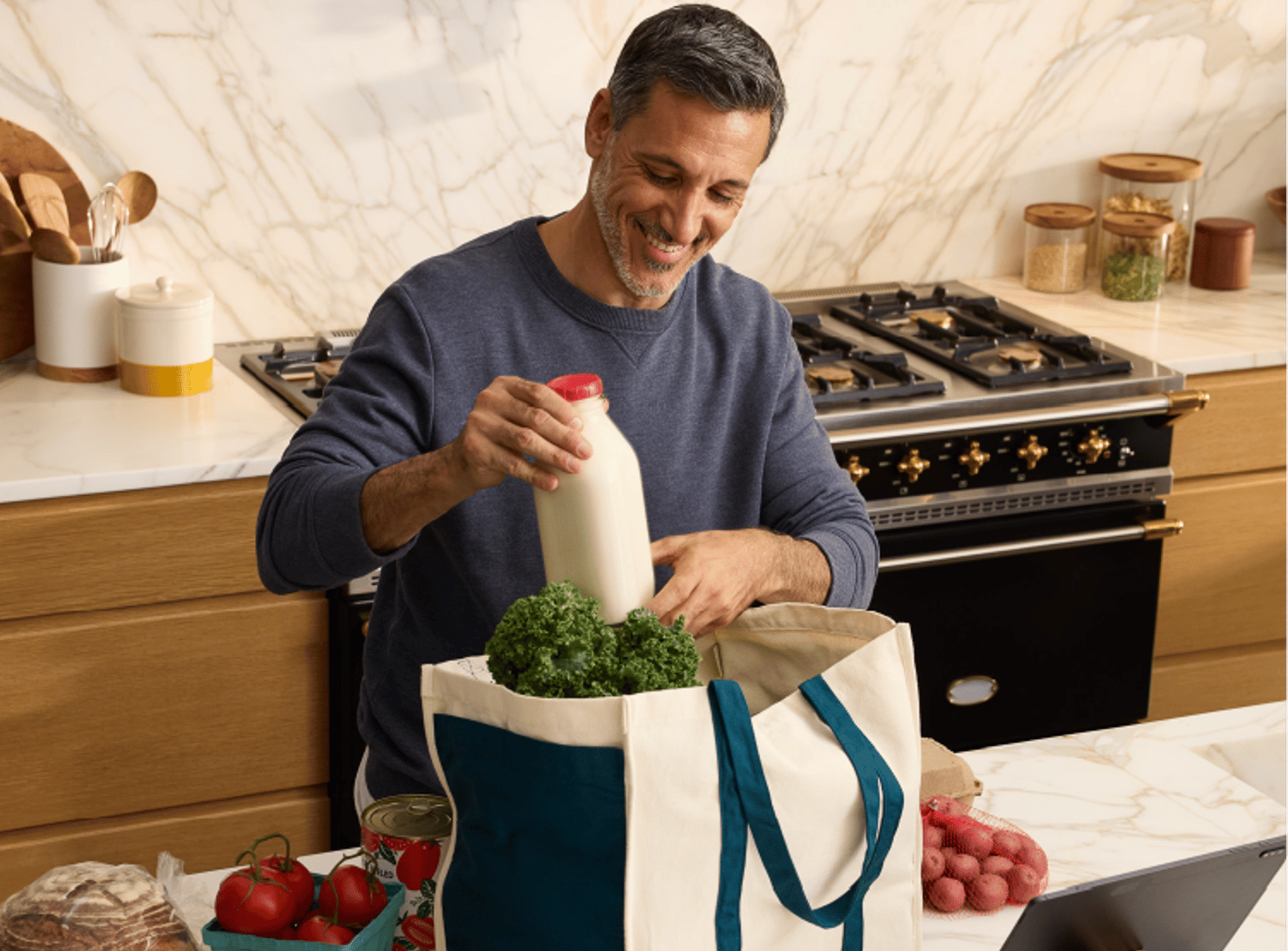 Image of a man pulling groceries out of a tote bag, in his kitchen with the FreshDirect logo locked in the top left corner