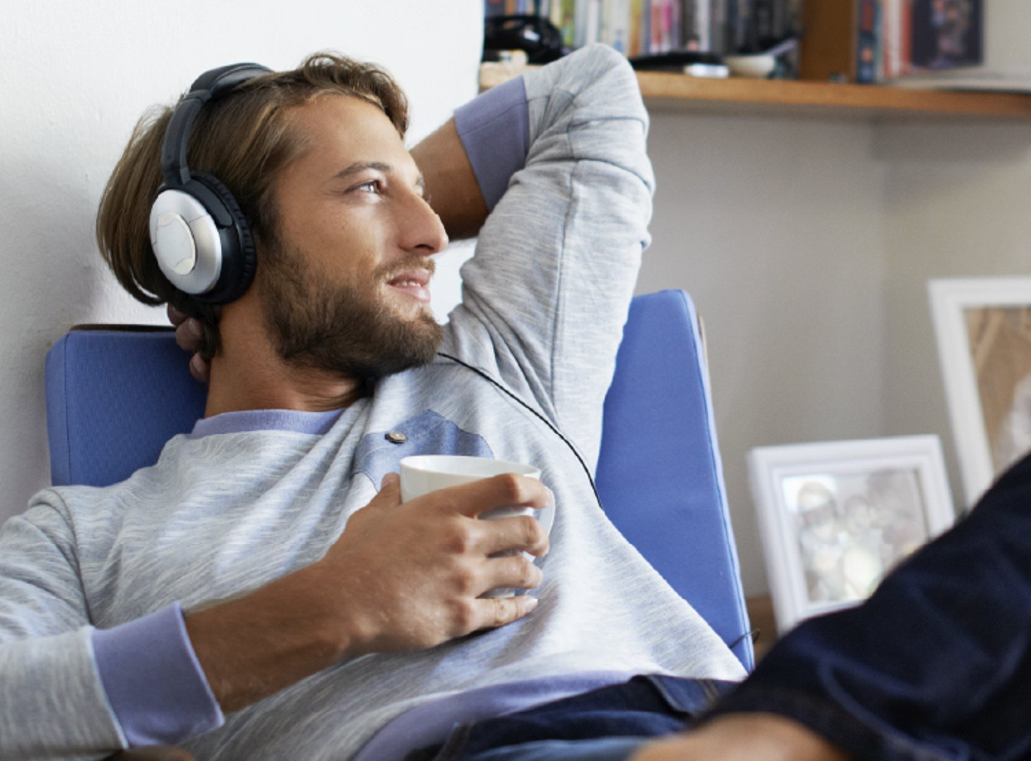 A man relaxing on a chair, wearing headphones and holding a cup, with a content expression.