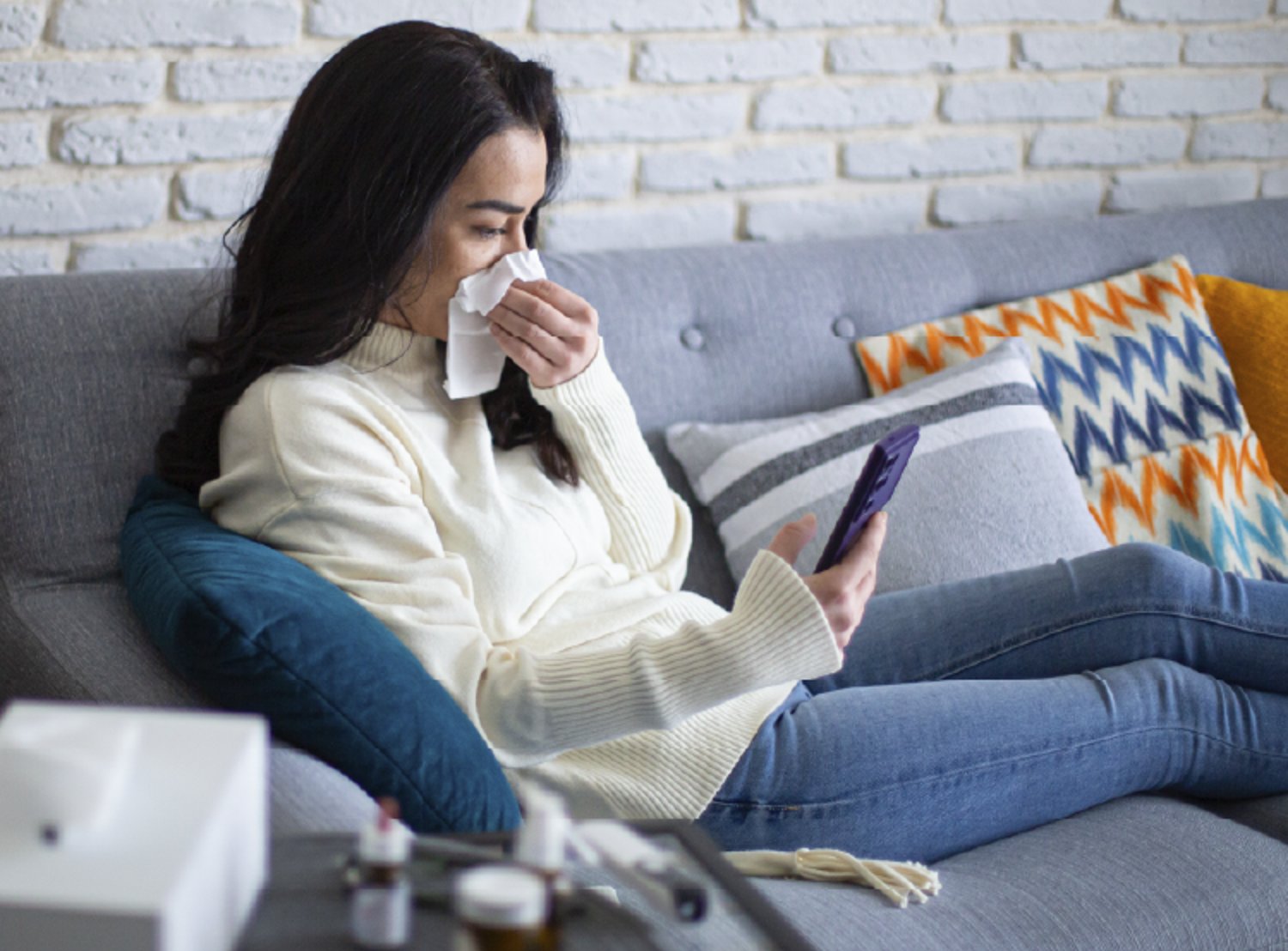 Woman sitting on sofa and blowing her nose into a tissue