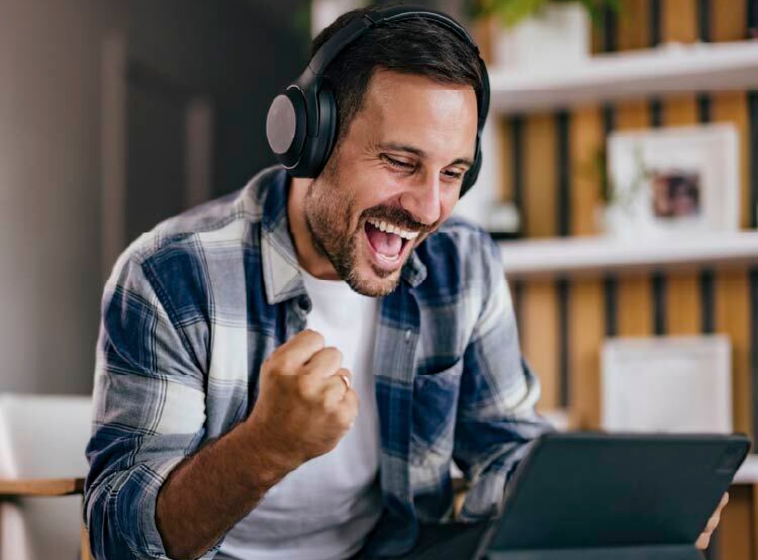 Man cheering while looking at a laptop and wearing headphones