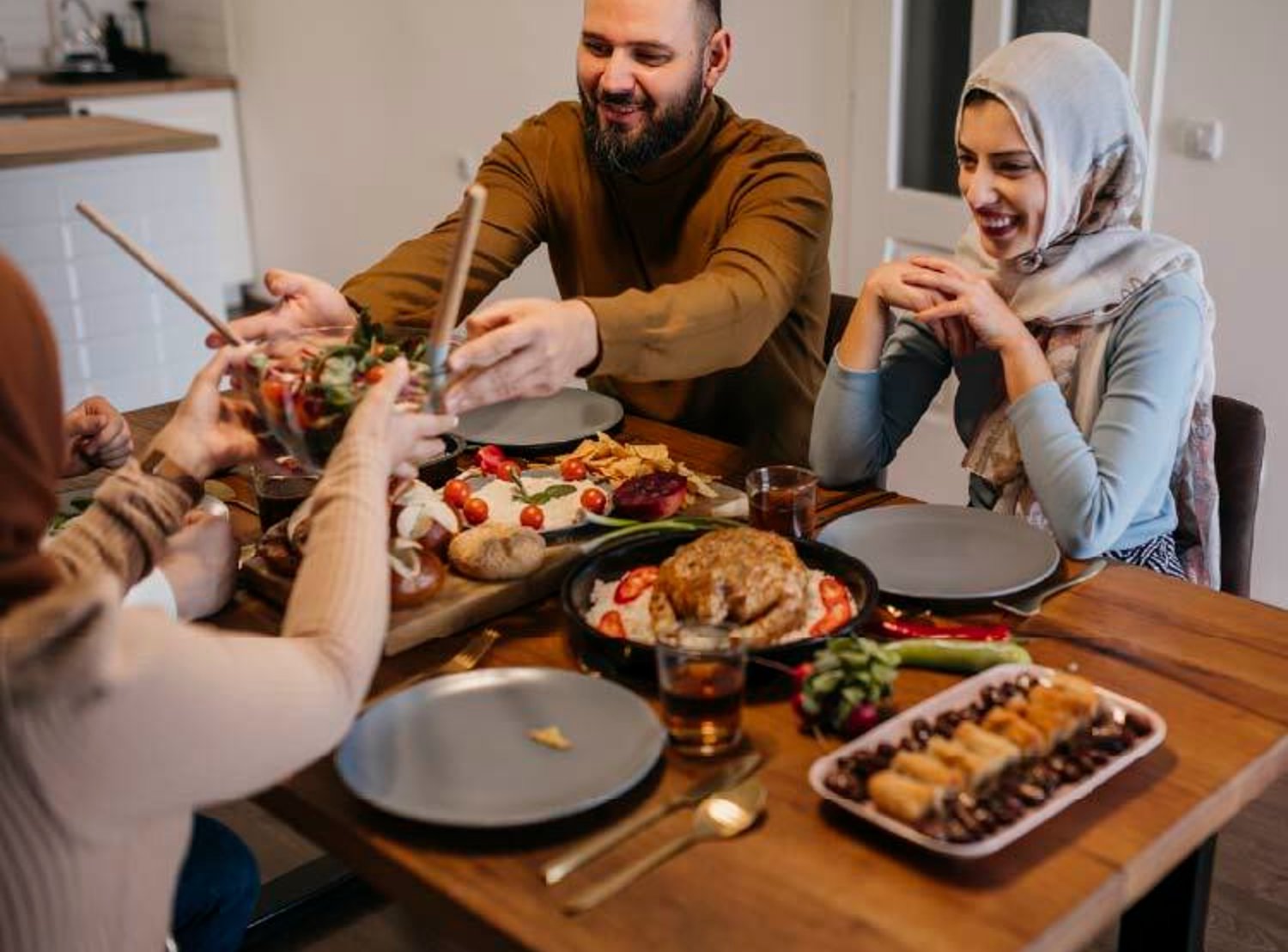 A warm and inviting family dinner scene with people sharing food at a wooden table, featuring a variety of dishes including salad, bread, and a main course.