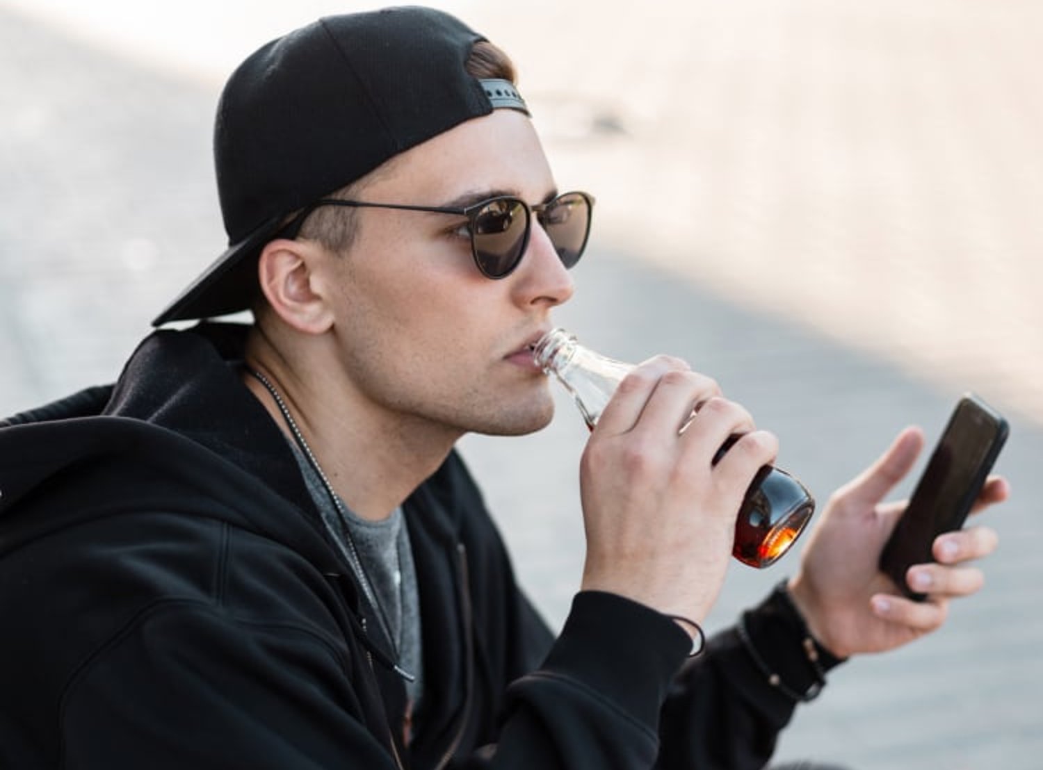 Image shows man sipping from a Pepsi bottle with his phone in hand