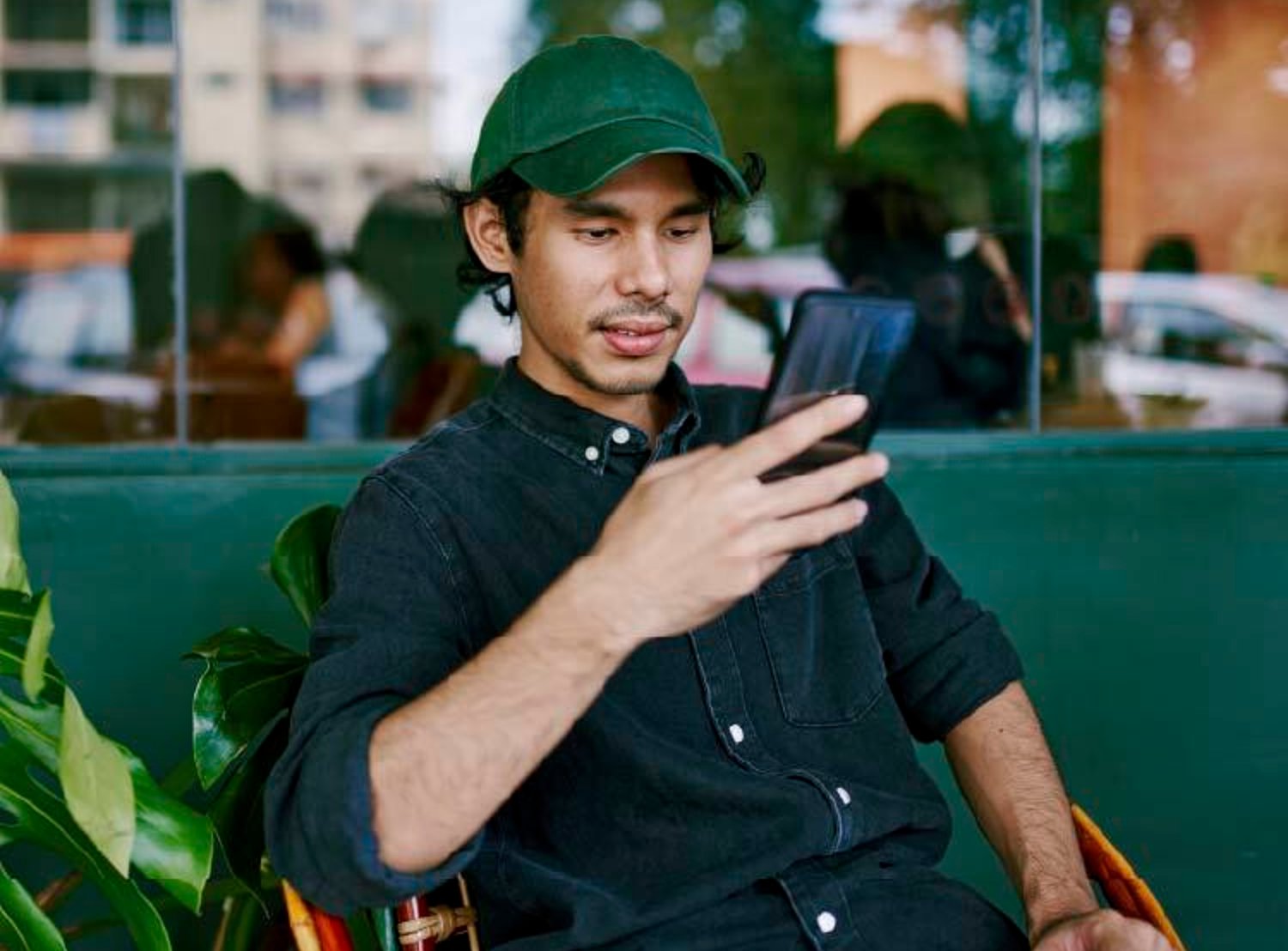 Man wearing a green hat, while staring at his phone